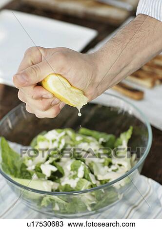 Stock Image - Man squeezing lemon over salad. Fotosearch