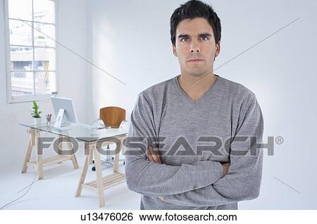Stock Photograph - Man standing in an office arms crossed. Fotosearch
