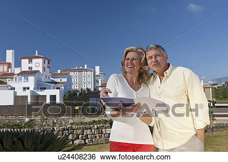 Stock Photograph - Mature couple holding realestate booklet. Fotosearch