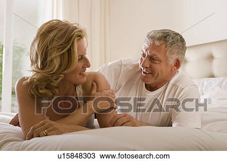 Stock Image - Mature couple lying on bed, talking. Fotosearch
