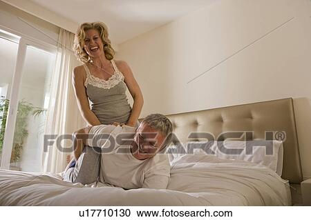 Stock Image - Mature couple wrestling on bed. Fotosearch