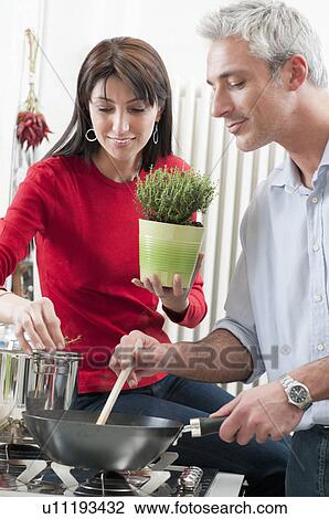 Stock Image - Mid aged couple cooking together. Fotosearch