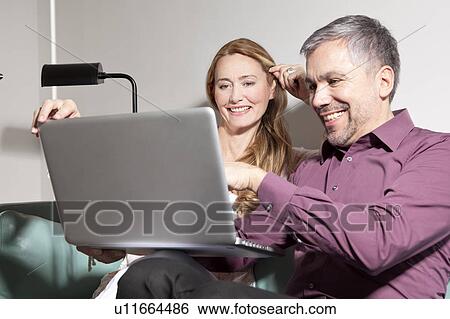Stock Photograph - Middle aged man and woman using laptop. Fotosearch