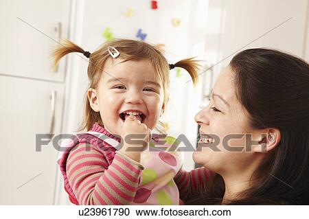 Stock Image - Mother and daughter laughing in kitchen. Fotosearch