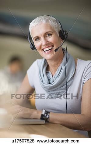Stock Photo - Older woman in headset using laptop. Fotosearch