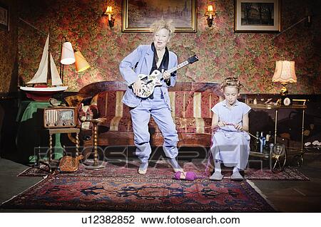 Stock Image - Older woman playing guitar as girl knits. Fotosearch