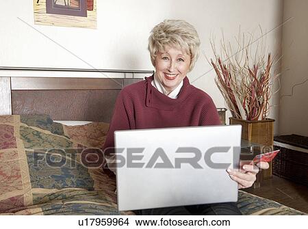 Picture - Older woman using laptop on bed. Fotosearch