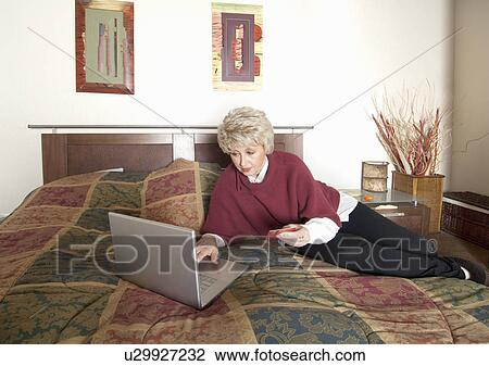 Older woman using laptop on bed View Large Photo Image Stock Image - Older woman using laptop on bed. Fotosearch