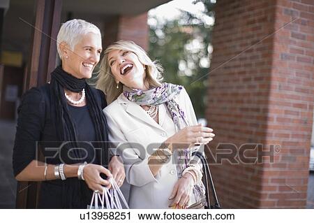 Stock Image - Older women carrying shopping bags. Fotosearch