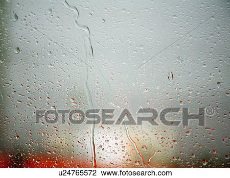 Stock Image - Rain droplets on window, red bus behind. Fotosearch