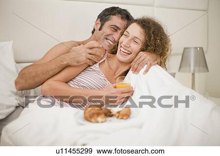 Smiling couple having breakfast in bed View Large Photo Image Stock Photo - Smiling couple having breakfast in bed. Fotosearch