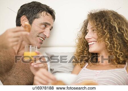 Smiling couple having breakfast in bed View Large Photo Image Stock Photo - Smiling couple having breakfast in bed. Fotosearch