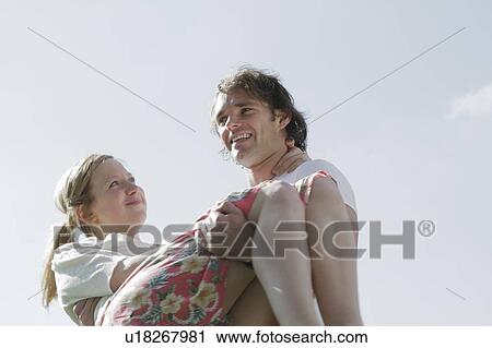 Stock Image - Smiling man carrying girlfriend. Fotosearch