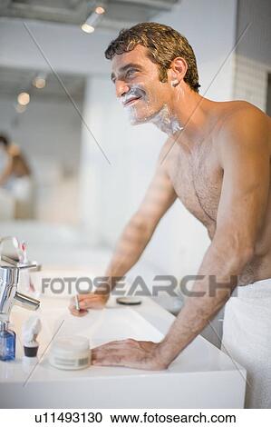 Stock Image - Smiling man shaving in bathroom. Fotosearch