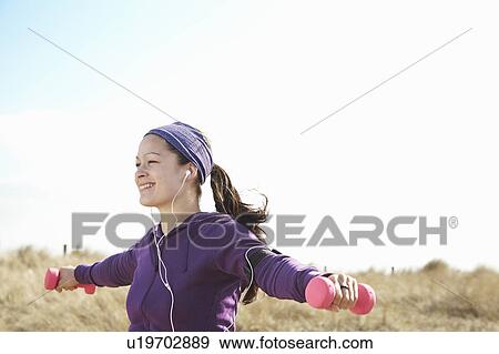 Stock Photo - Smiling woman lifting dumbbells outside. Fotosearch