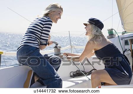 Stock Image - Smiling women sailing on boat. Fotosearch
