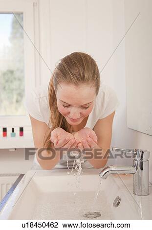 Stock Image - Teenage girl washing face in bathroom. Fotosearch