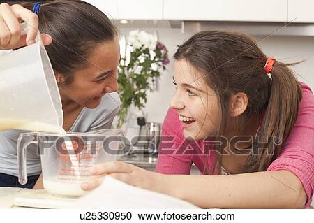 Stock Image - teenage girls measuring milk in kitchen. Fotosearch