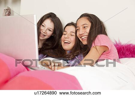 Stock Image - teenage girls sitting in bed with feet out of the cover. Fotosearch