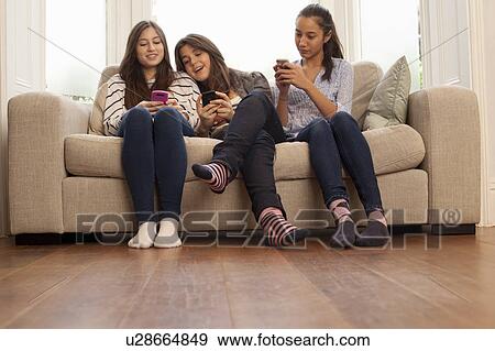 Stock Photo - teenage girls sitting on sofa looking at phones. Fotosearch
