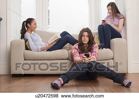 Stock Photo - teenage girls sitting on sofa reading, checking messages. Fotosearch