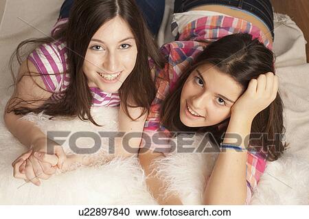 Stock Image - teenage girls smiling, lying on pillows. Fotosearch