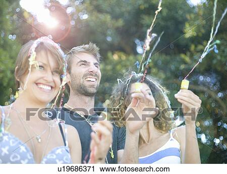 Stock Image - Three friends letting off party poppers. Fotosearch