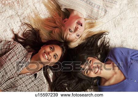 Stock Photo - Three young women lying on white rug. Fotosearch