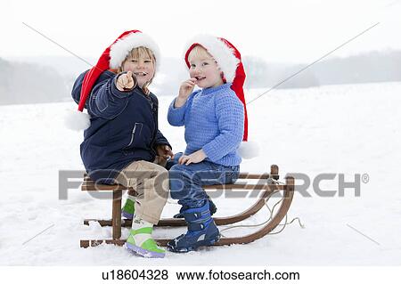 Stock Photo - Two boys on a sledge wearing Xmas hats. Fotosearch