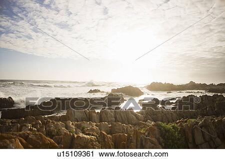 Stock Image - Waves crashing over rocks on beach. Fotosearch
