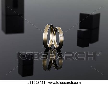 Stock Image - Wedding rings on reflective surface. Fotosearch