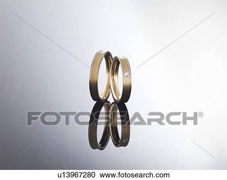 Stock Image - Wedding rings on reflective surface. Fotosearch