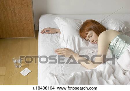 Picture - woman asleep in bed with tablets. Fotosearch