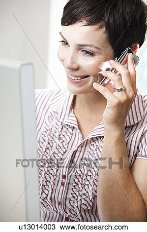 Stock Image - Woman at computer with phone. Fotosearch