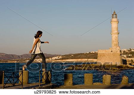 Stock Photography - woman balancing on stones in front of a lighthouse. Fotosearch