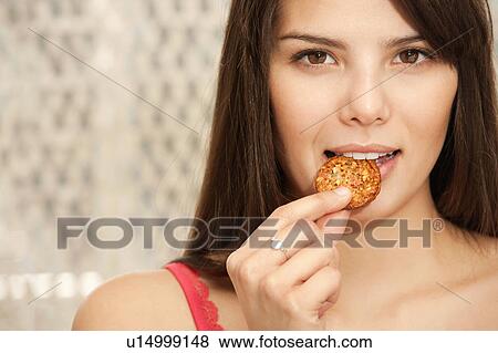 Stock Photo - Woman biting a biscuit half smiling. Fotosearch