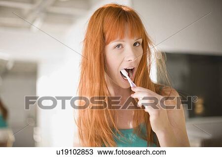 Stock Image - Woman brushing her teeth in bathroom. Fotosearch
