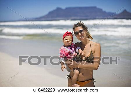 Stock Photo - Woman carrying baby girl on beach. Fotosearch