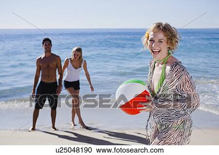 Stock Image - Woman carrying ball on beach. Fotosearch