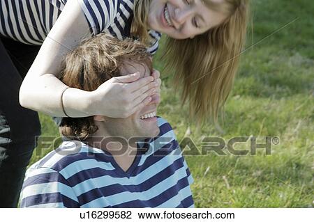 Stock Image - Woman covering boyfriend’s eyes. Fotosearch