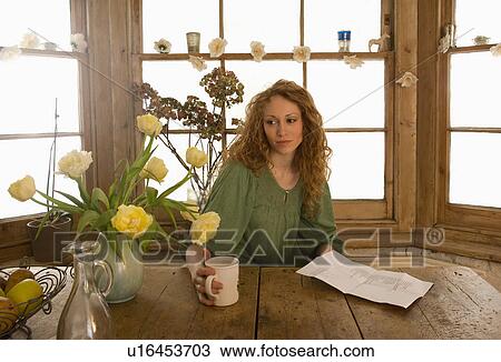 Stock Image - Woman drinking coffee at kitchen table. Fotosearch