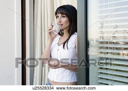 Woman drinking water at window View Large Photo Image Picture - Woman drinking water at window. Fotosearch