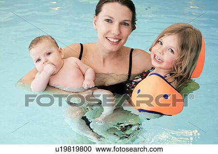 Stock Image - Woman holding children in swimming pool. Fotosearch