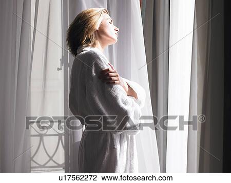 Stock Image - Woman in bath robe by the window. Fotosearch