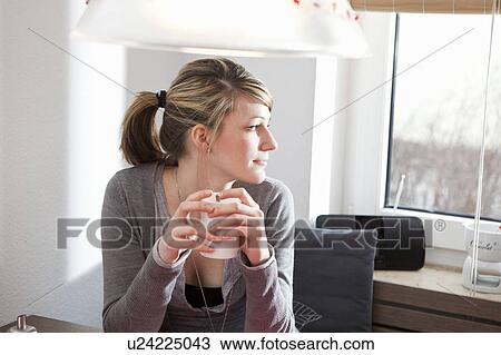 Stock Image - Woman in kitchen, looking out the window. Fotosearch