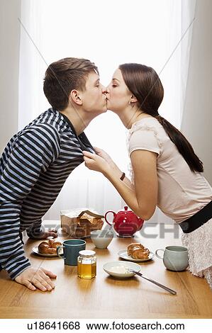 Stock Photo - Woman kissing boyfriend ove table. Fotosearch