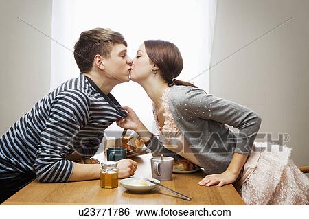 Stock Photograph - Woman kissing boyfriend over table. Fotosearch