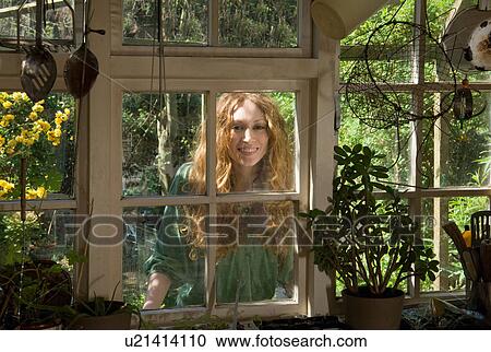 Stock Image - Woman looking through kitchen window. Fotosearch