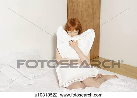 Stock Image - woman on bed hugging pillow. Fotosearch
