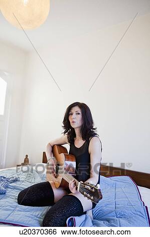 Stock Photograph - Woman playing guitar on bed. Fotosearch